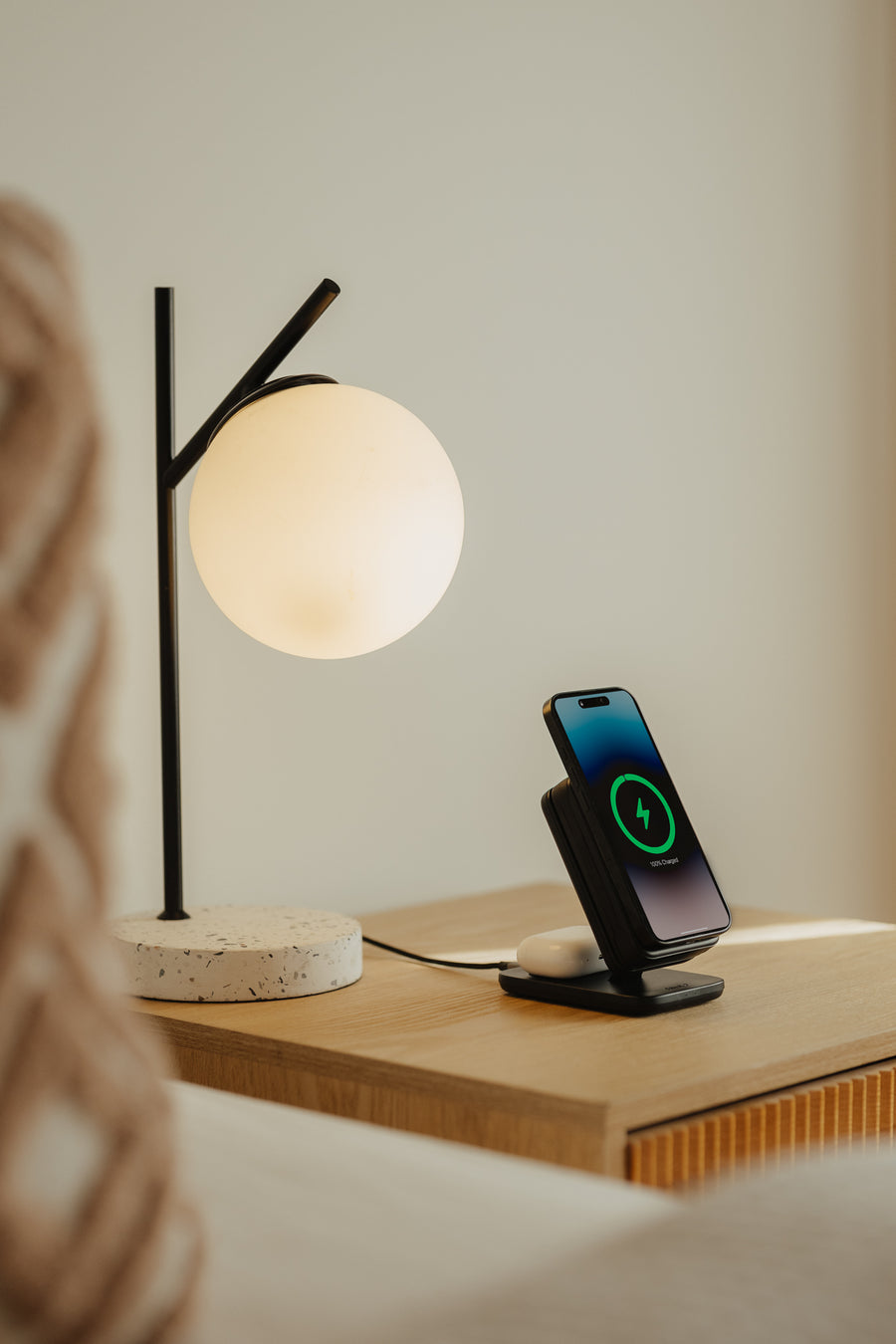 A phone charging on top of the PowerDock 2 on a bedside table
