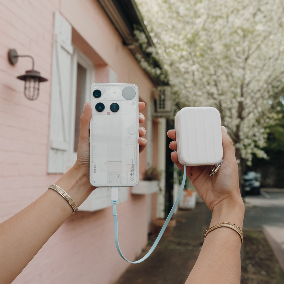 White PowerPack Mini 2 charging a phone through its retractable USB-C cable outdoors.