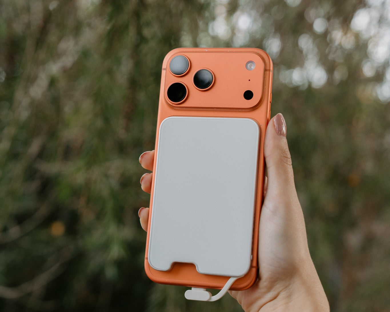 PowerPack Slim 3 magnetic power bank attached to an orange smartphone held outdoors