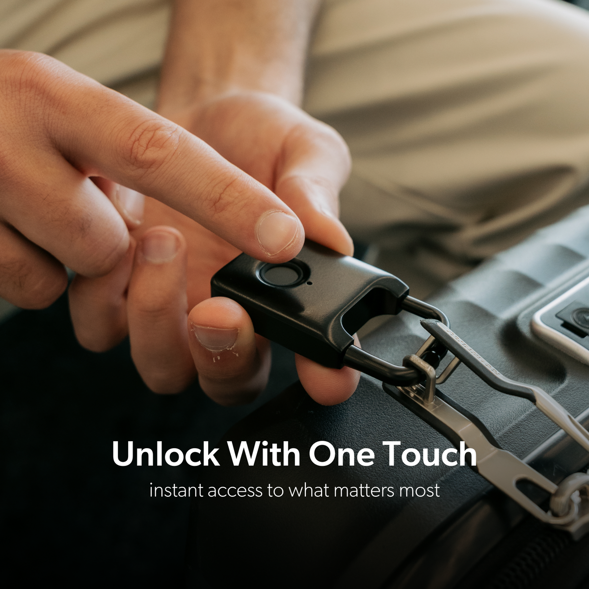 A finger touching the sensor on a black Trvlr Lock beside suitcase zipper pulls.