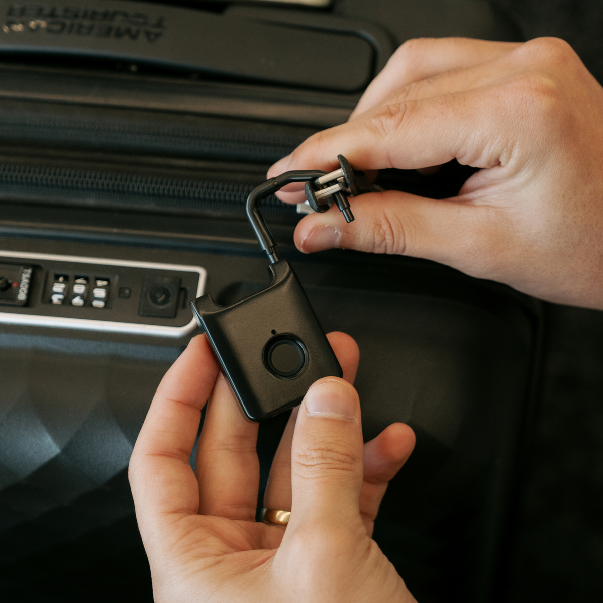 Hands fastening a black Trvlr Lock through suitcase zipper pulls.
