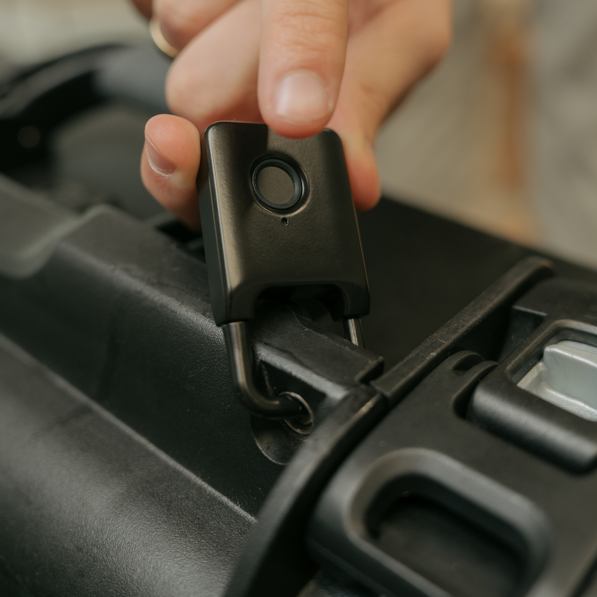 Close-up of a finger pressing the Trvlr Lock fingerprint sensor beside a suitcase handle.